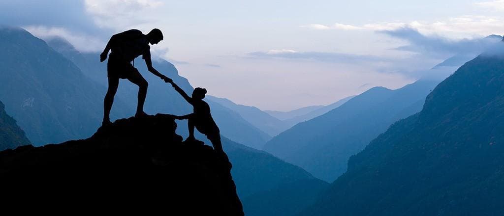 Deux silhouettes en montagne, l'une tendant la main à l'autre